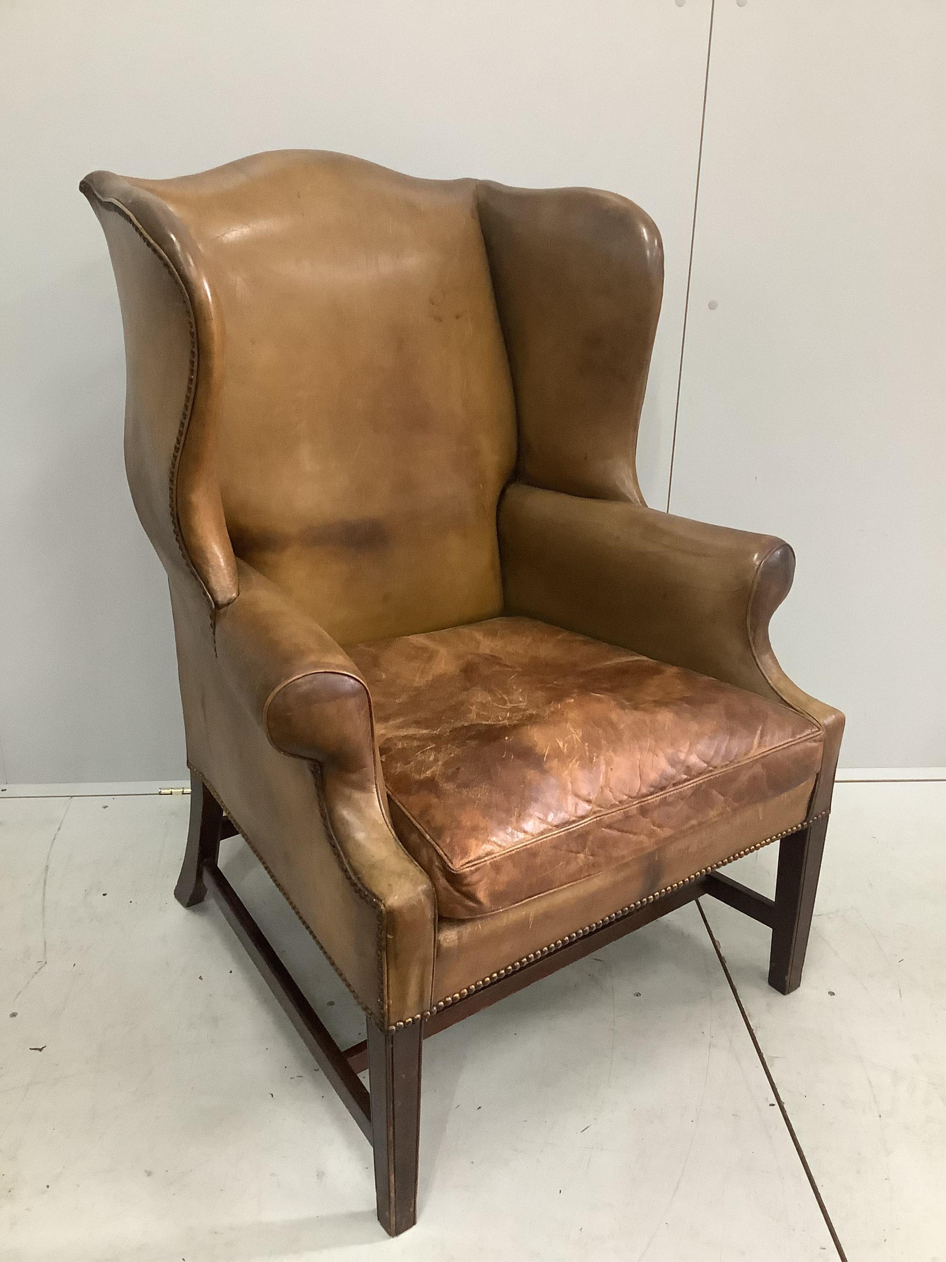 A George III style tan leather wing armchair, width 80cm, depth 68cm, height 107cm. Condition - fair